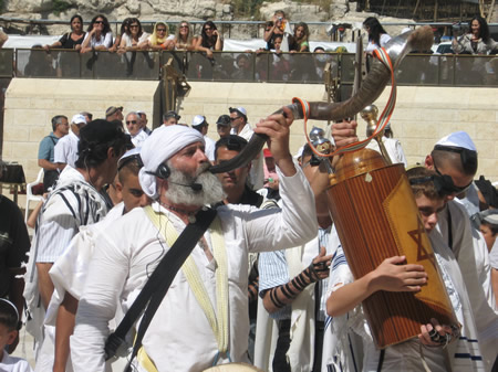 A shofar is played at a bar mitzvah at the Western Wall as the young man carries a copy of the law with a group of men into Wilson’s Arch as the women watch from behind the separation barrier.