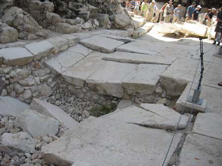 Crushed pavement along the Western Wall. The falling stones from the Temple Mount above in the 70 AD broke through this pavement that covers a gutter below. The curb of the street and the shops along the street can be seen in the top left corner. 