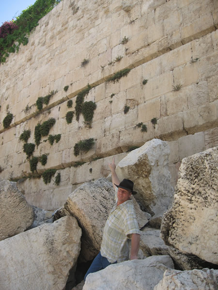 Galyn stands among the fallen stones from the Temple Mount and points to where they were pushed from by the Romans in 70 AD